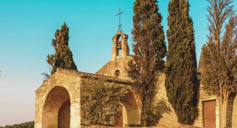 Chapelle romane en pierre avec clocher mur entouree de cypres au soleil couchant
