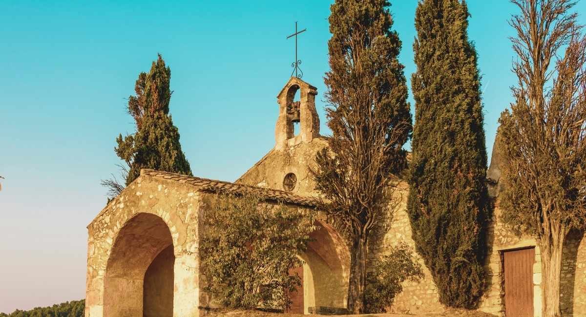 Chapelle romane en pierre avec clocher mur entouree de cypres au soleil couchant