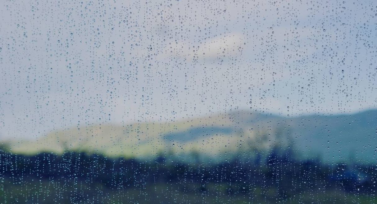 Gouttes de pluie sur une vitre avec des collines floues en arrière-plan