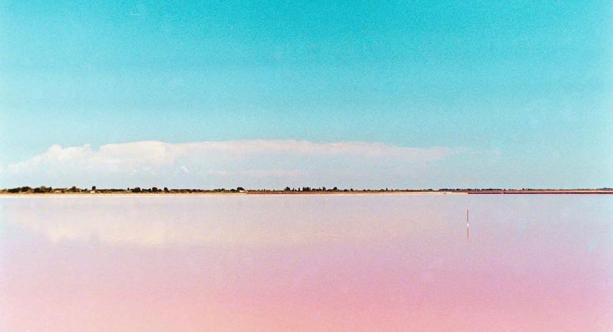 Eaux roses et immobiles des marais salants d'Aigues-Mortes sous un ciel bleu