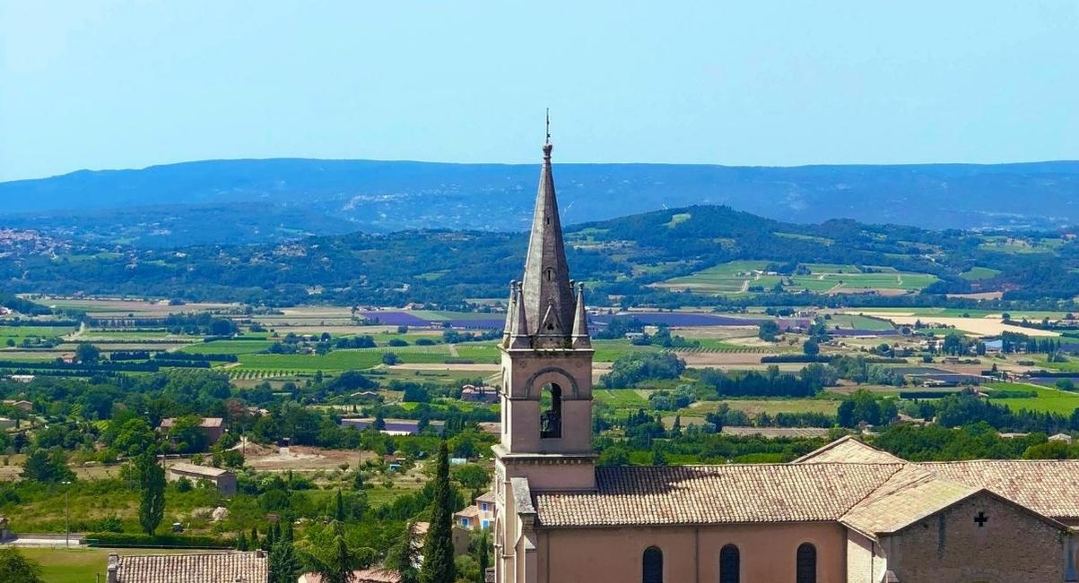 Clocher d'une église de village dominant la vallée et les champs du Luberon